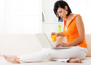 Woman on her couch typing on a laptop.