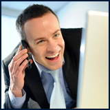A picture of a man talking on the phone while using his laptop computer.